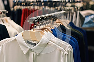 Woman shirts amd blouses in white, blue, black and other colors on hangers in a retail clothes store.