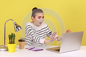 Woman with shocked expression raising hands in stop gesture, working on laptop, prohibited content