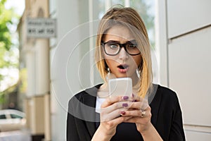 Woman shocked with sms message on phone. Closeup woman girl looking at cellphone stunned surprised face, black suit formal wear,