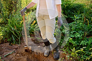 Woman shod in boots shoveling in her backyard