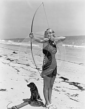 Woman shooting bow and arrow on beach