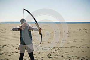 Woman shooting target with her bow and arrow on a sunny day on the beach.