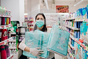 Woman shopper with mask and gloves panic buying and hoarding disposable diapers.Preparing for pathogen virus pandemic quarantine.