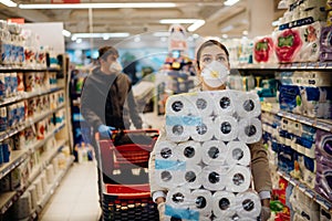 Woman shopper with mask and gloves panic buying and hoarding toilette paper in supply store.Preparing for pathogen virus pandemic