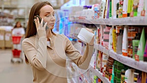 Woman shopper in a supermarket, cheerfully talking on a mobile phone, choosing goods