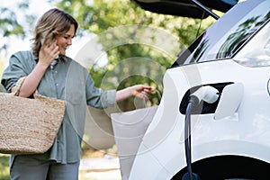 Woman with shopping bag next to a charging electric car