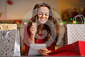 Woman among shopping bags checking list in Christmas kitchen