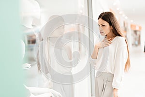 Woman in shopping mall. Girl is standing near store window looking at new dress.