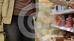 Woman with shopping basket choosing refrigerated groceries at the supermarket.