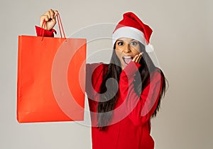 Woman shopping for christmas gifts with shopping bags and santa hat looking excited and happy