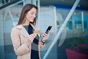 Woman shopping with credit card. Beautiful young lady with gold card using phone