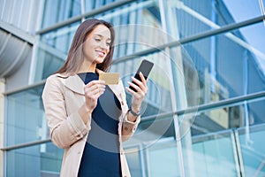 Woman shopping with credit card. Beautiful young lady with gold card using phone