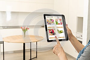 Woman shopping food online using a digital tablet at the kitchen, close-up view on a tablet screen. Concept of buying