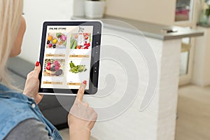 Woman shopping food online using a digital tablet at the kitchen, close-up view on a tablet screen. Concept of buying