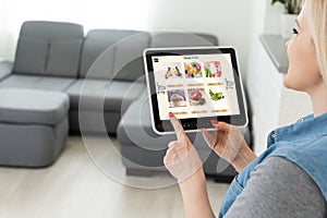 Woman shopping food online using a digital tablet at the kitchen, close-up view on a tablet screen. Concept of buying