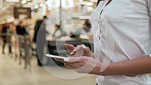 Woman shopping food in supermarket background. Close up view girl buy products using digital gadget in store. Hipster at