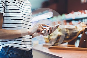 Woman shopping healthy food in supermarket background. Close up view girl buy products using digital gadget in store. Hipster