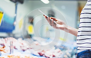 Woman shopping healthy sea food in supermarket background. Close up view girl buy products using digital gadget in store. Hipster