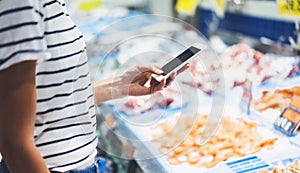 Woman shopping healthy sea food in supermarket background. Close up view girl buy products using digital gadget in store. Hipster