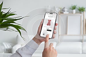 Woman shopping online with smart phone. Buying a red flow dress on ecommerce web page. Living room interior in background photo