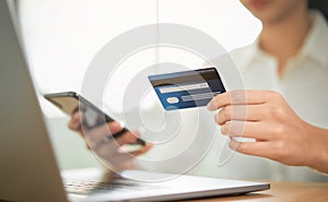 Woman shopping online on smartphone and holding back view of the credit card and enter the payment code for the product.