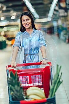 Woman shopping in supermarket pushing trolley and smilling