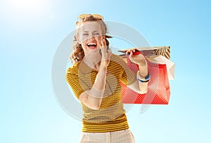 Woman with shopping telling exciting news against blue sky