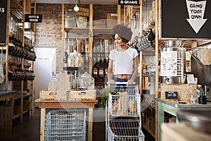 Woman With Shopping Trolley Buying Fresh Fruit And Vegetables In Plastic Free Grocery Store