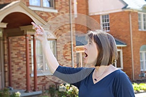 Woman with short hair in front of blurred brick houses points and looks surprised