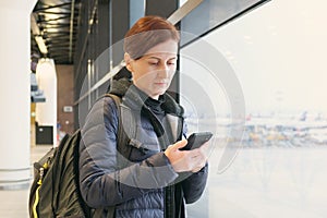 Woman with short hair holds a smartphone in her hands and looks at the screen while waiting for her flight