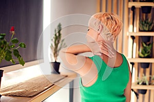 Woman with short hair with neck and shoulder pain and injury, back view, close up. Female hands on suffered muscles. Health care