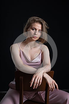 Woman with short hair posing in pink suit, sitting on chair on black background