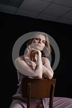 Woman with short hair posing in pink suit, sitting on chair on black background