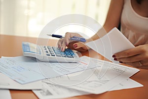 Woman with short sleeved t shirt with a calculator figuring out bills spread out on a wooden table