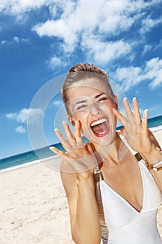 Woman shouting through megaphone shaped hands at sandy beach