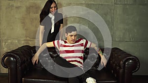 A woman shouts and yells at the man sitting on the couch. In this case, the male is not forced to sit and does not pay