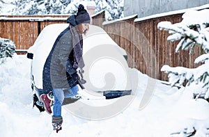 woman with shovel cleaning snow around car. Winter shoveling. Removing snow after blizzard