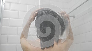 Woman in the shower, back side of young female showering under refreshing water, healthy lifestyle. Girl washing long