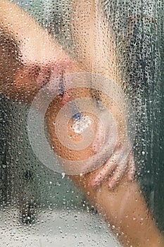 Woman in the shower shaves. Sexy young woman shaving her leg in shower cabin. Close-up view of female leg with razor. Girl hand
