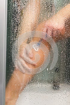 Woman in the shower shaves. Sexy young woman shaving her leg in shower cabin. Close-up view of female leg with razor. Girl hand