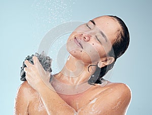 Woman, shower and water drops with loofah in hygiene, grooming or washing against a blue studio background. Female