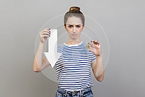 Woman showing of bitcoin and white arrow pointing down, expressing negative emotions.