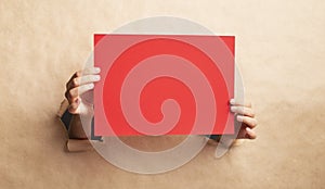 Woman showing blank red sheet through hole in craft paper, mockup for design