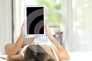 Woman showing blank tablet screen lying in bed