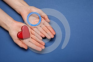 Woman showing blue paper circle as World Diabetes Day symbol and red heart on color background, top view with space for text