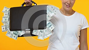 Woman showing brief case full of money into camera, start-up investing capital