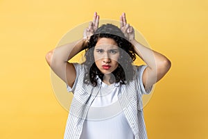 Woman showing bull horn gesture with fingers over head, looking hostile and threatening.