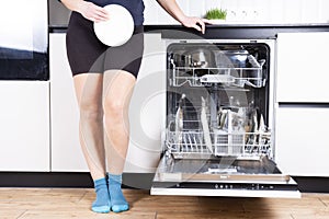 Woman is showing the clean plate with dishwasher in dirty kitchen, cropped image