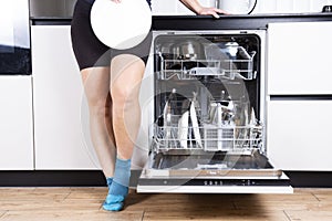 Woman is showing the clean plate with dishwasher in white dirty kitchen, cropped image
