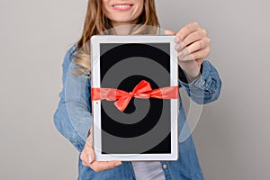 Woman showing digital tablet with red ribbon gift isolated on grey background pad pda modern technology people person concept free